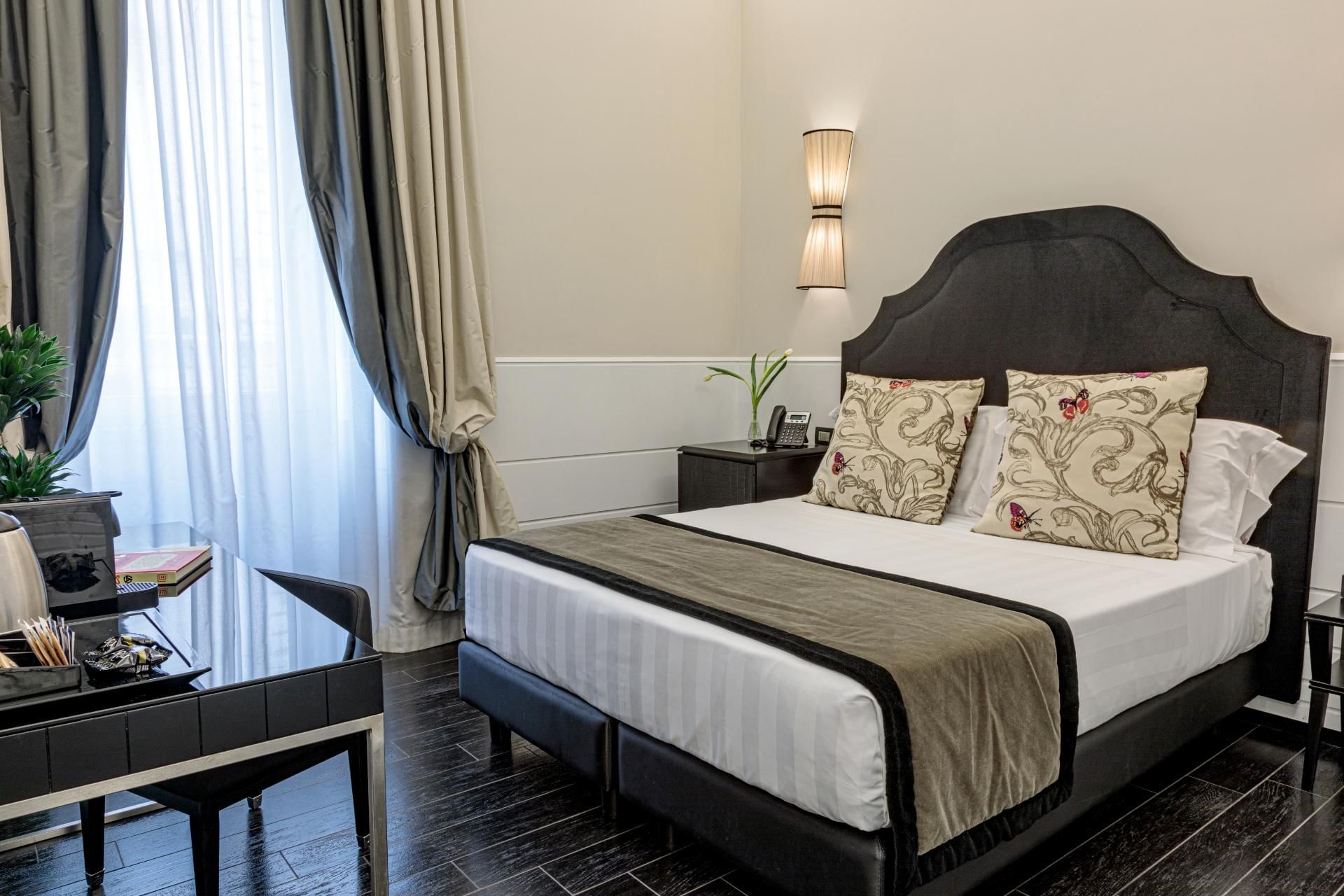 Stylish Smart Room at The Independent Suites with a double bed, modern lamp, desk, and soft natural light through curtains