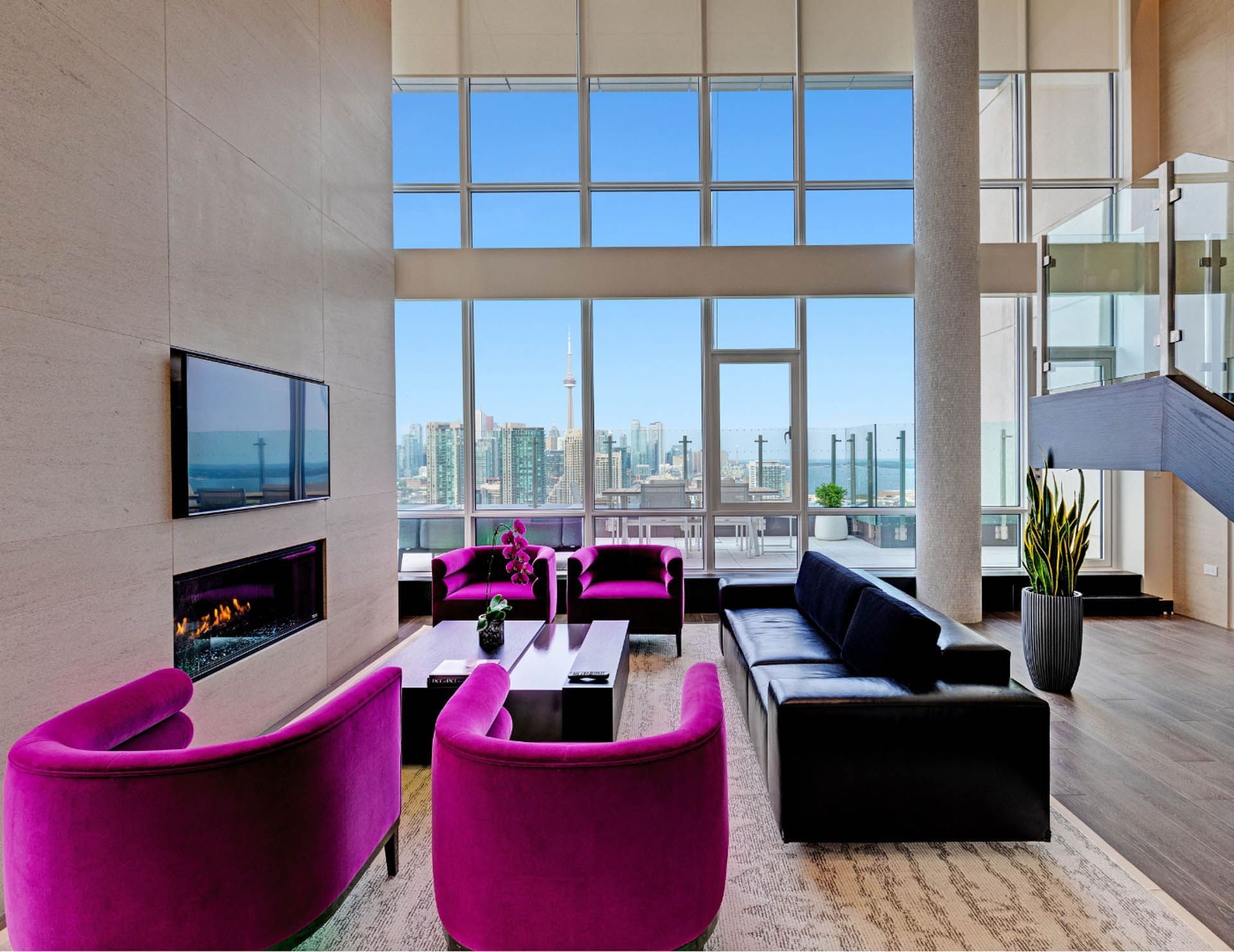 Modern suite lounge with armchairs and black sofa beside fireplace facing city view with CN Tower at Hotel X Toronto