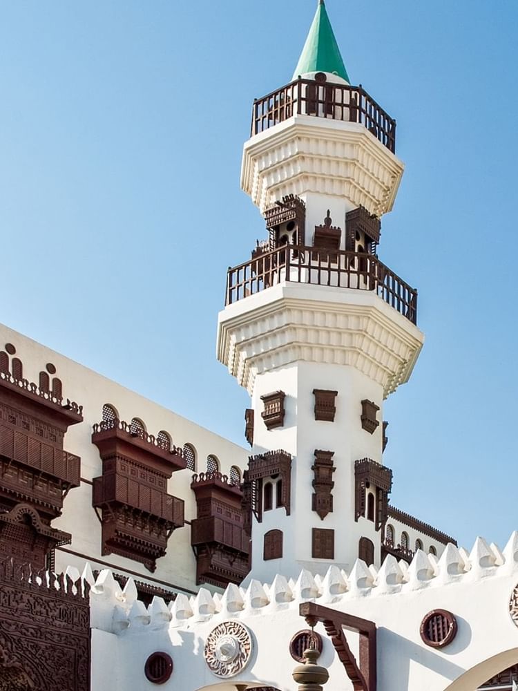 Jeddah with a tall minaret and green domes by ornate wooden balconies near Warwick Hotels & Resort