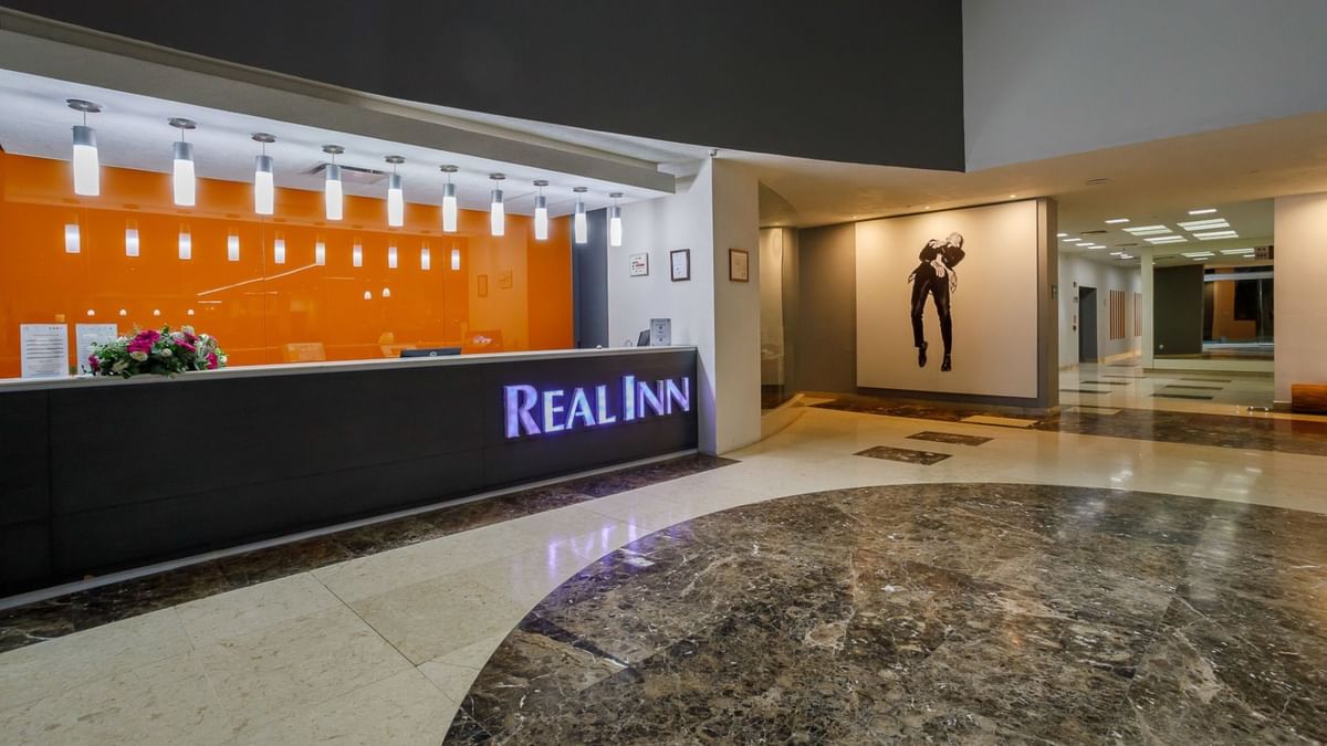 Professional reception area with a dark wood desk and warm orange accent lighting at Real Inn Tijuana