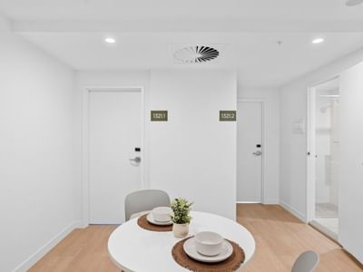 White room with round table and two chairs at UniLodge Brisbane City.