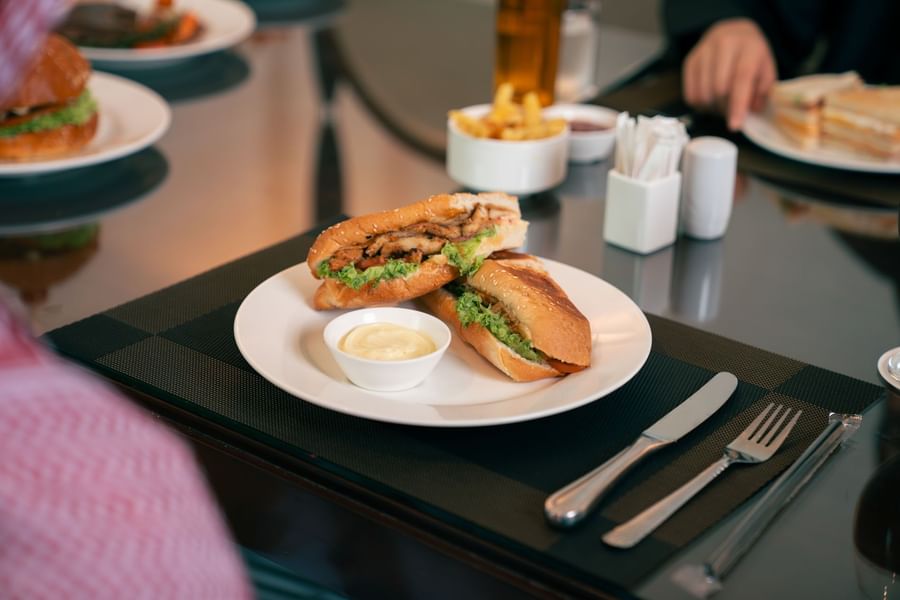 Delicious toasted chicken sandwich served with a side of creamy dip on a white plate at Saja by Warwick Makkah