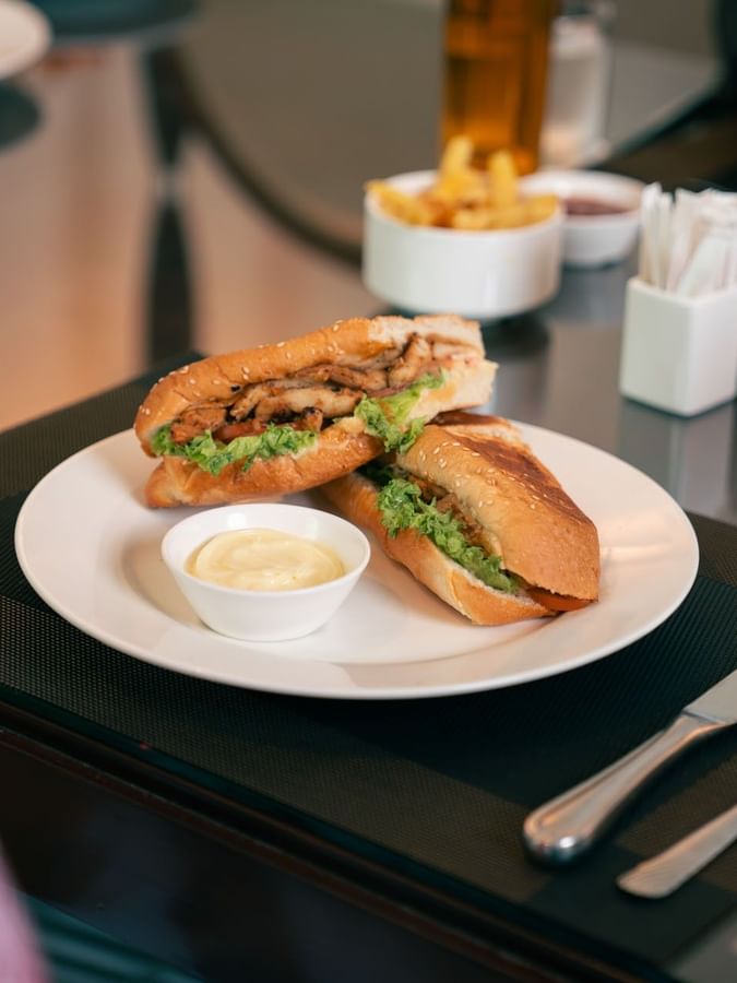 Toasted chicken sub sandwich served with creamy dip and golden fries on a white plate at Saja by Warwick Makkah