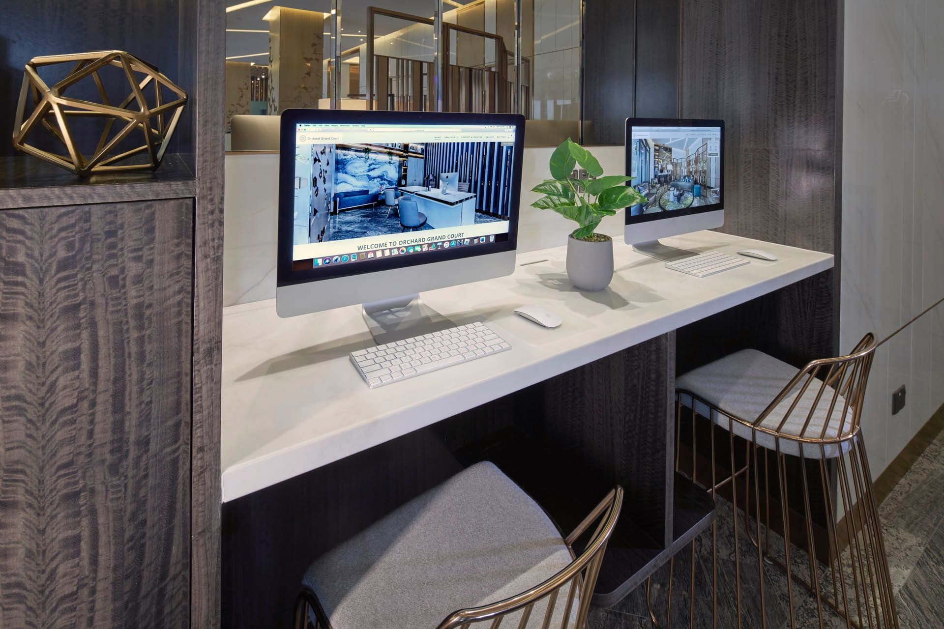 Two iMacs on a sleek white desk with wire chairs, and a geometric sculpture in Lobby Business Center at Orchard Grand Court