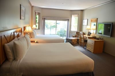 Two beds face the patio door, a lounge chair by the desk with a TV in Courtside Queen Executive at Hilltop Inn Salmon Arm