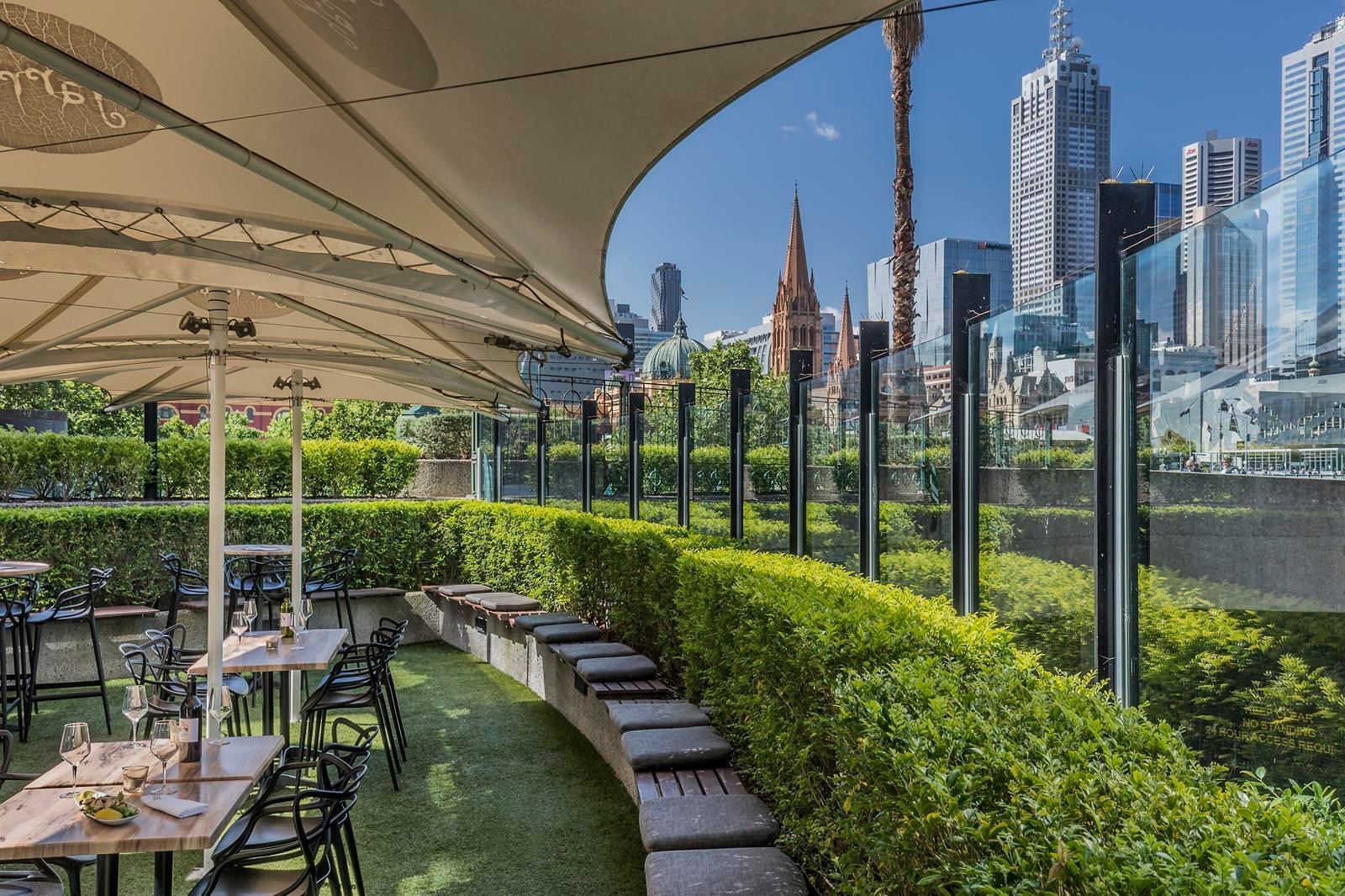 Open dining area arranged in Jarrah Bar & Terrace with a city view at Quay West Suites Melbourne
