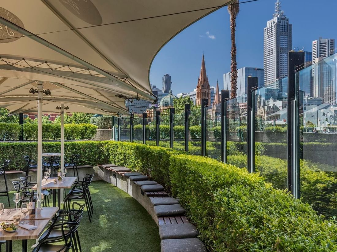 Open dining area arranged in Jarrah Bar & Terrace with a city view at Quay West Suites Melbourne