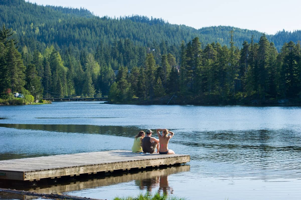People relaxing on the deck overlooking Alpha Lake near Blackcomb Springs Suites