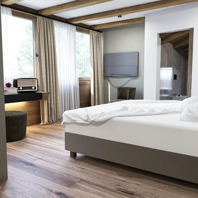 Geräumiges Schlafzimmer mit Holzboden, großem Bett, Nachttisch, Fernseher und angrenzendem Bad.