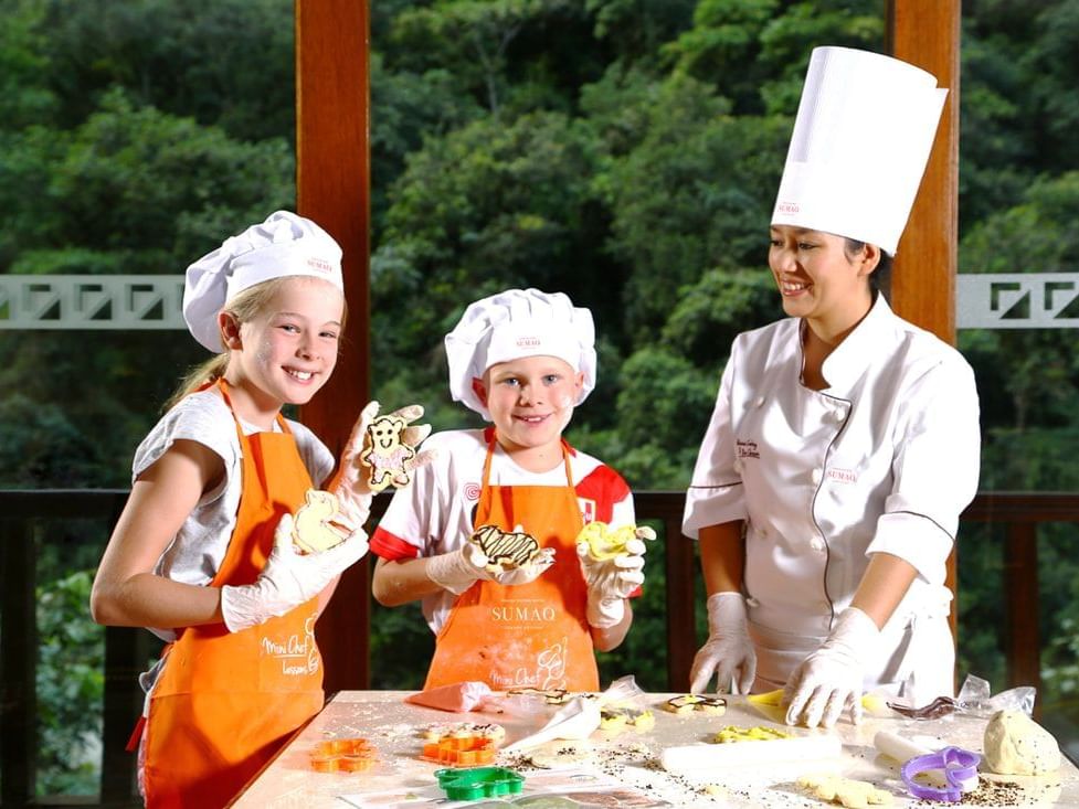 A chef and two kids in aprons making cookies at Hotel Sumaq