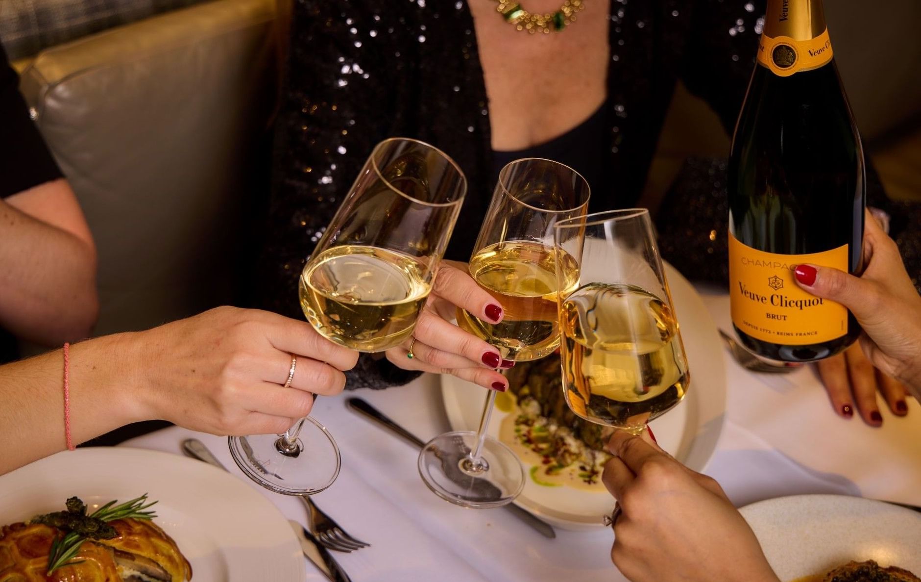 Nahaufnahme von Freunden, die mit Weingläsern neben einer Flasche Veuve-Clicquot-Champagner im „The Londoner Hotel“ anstoßen