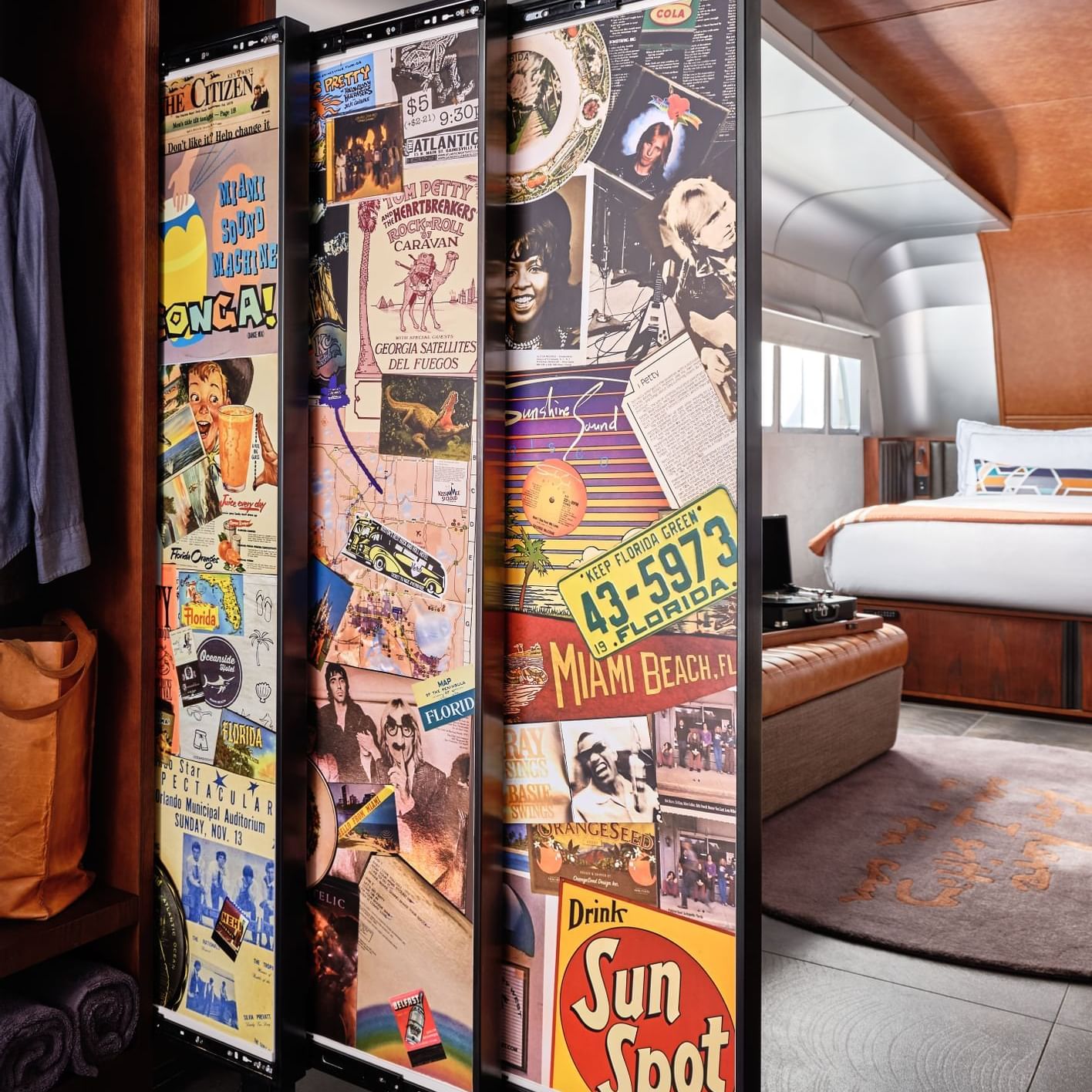 Vintage travel poster-covered room divider on wheels separates sleeping area in retro-styled hotel suite with curved ceiling