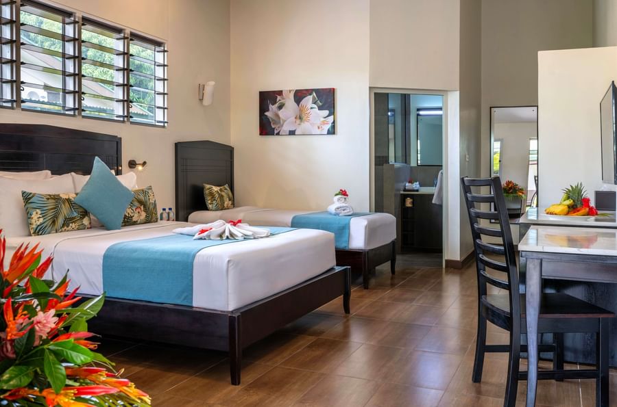 Two beds with tropical decor and a dining area in a resort room at Tokatoka Resort Fiji International Airport.