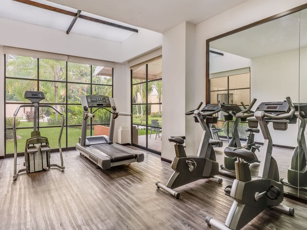 Gimnasio luminoso en Fiesta Inn Colima con cintas, bicicletas estáticas y ventanas al jardín exterior