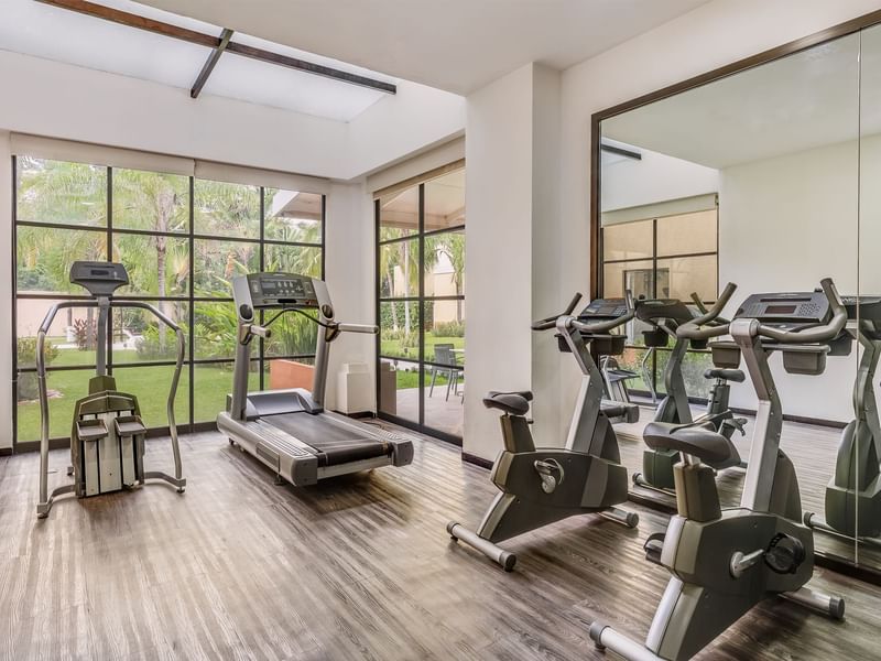 Gimnasio luminoso en Fiesta Inn Colima con cintas, bicicletas estáticas y ventanas al jardín exterior