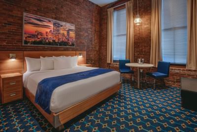 Bed with sunset art on a brick wall next to two windows with a table in King City View at Harborside Inn Boston