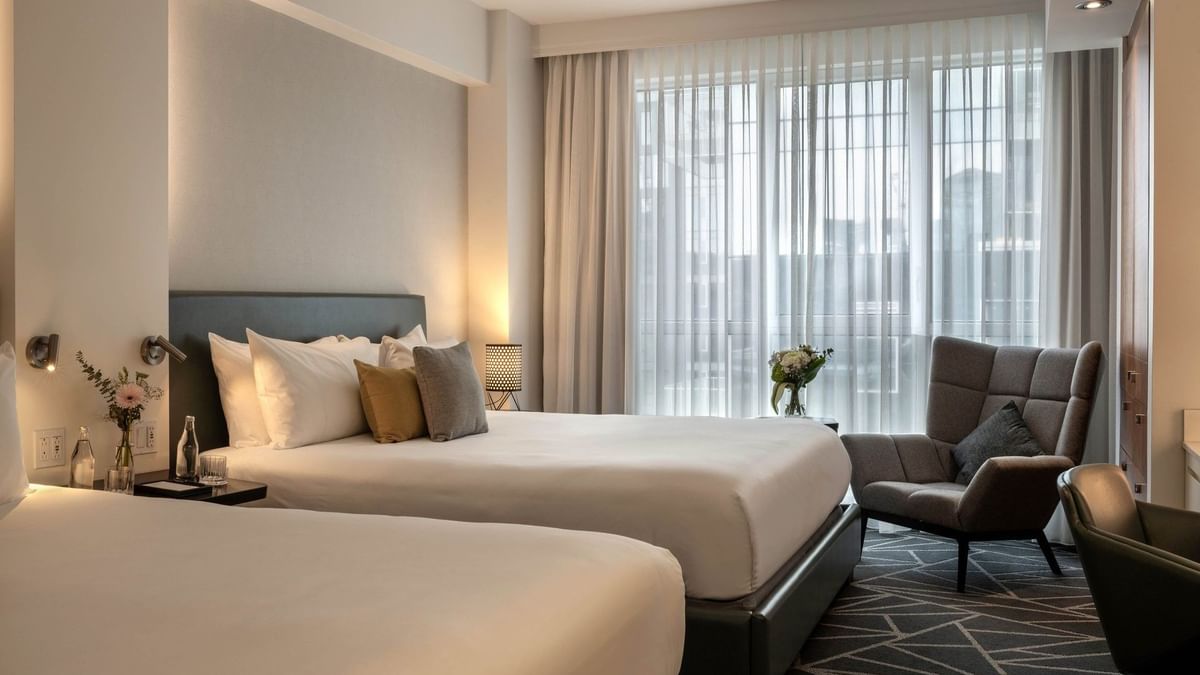 Deux lits king size, une décoration moderne et une fenêtre avec vue sur la ville dans la suite Loft du Warwick Le Crystal Montréal.