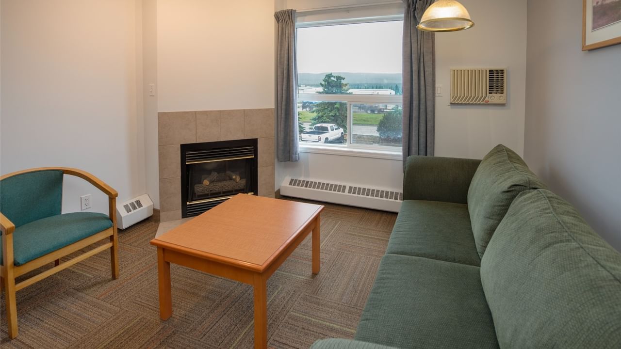 A cozy living room with a green couch, coffee table, chair, and fireplace, offering a scenic view.