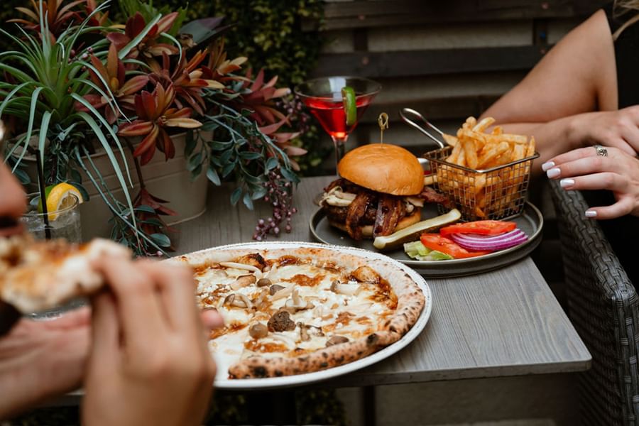 two people seating on the terrace and eating a pizza and a burger