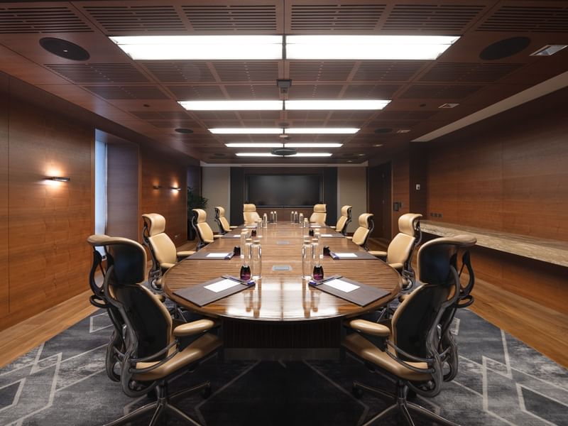 Modern executive boardroom with a sleek wooden table, high-back chairs, and natural light from large windows, perfect for corporate discussions.