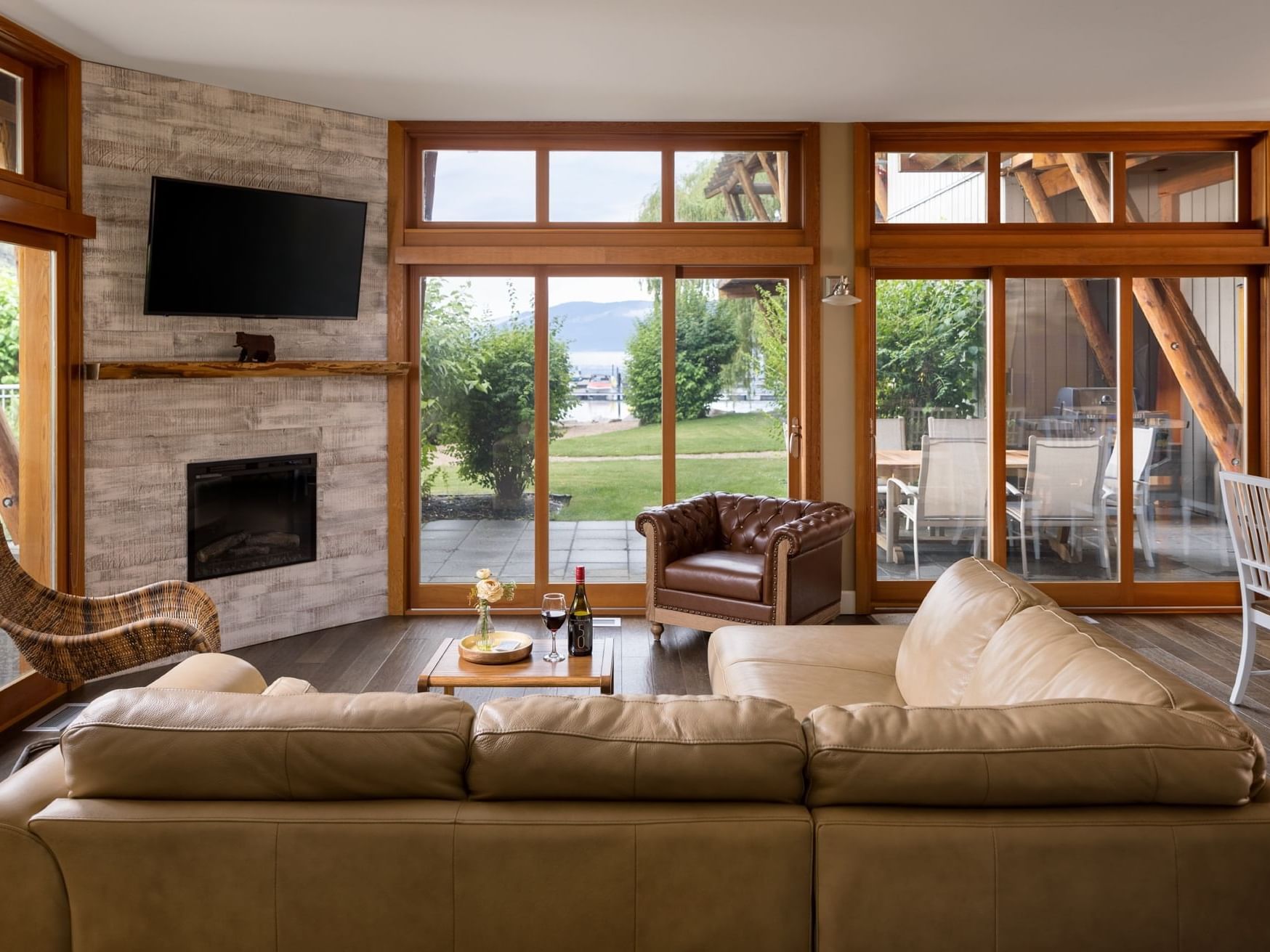 Living room with fireplace, leather couch, large windows, and dining area in a house with outdoor view.