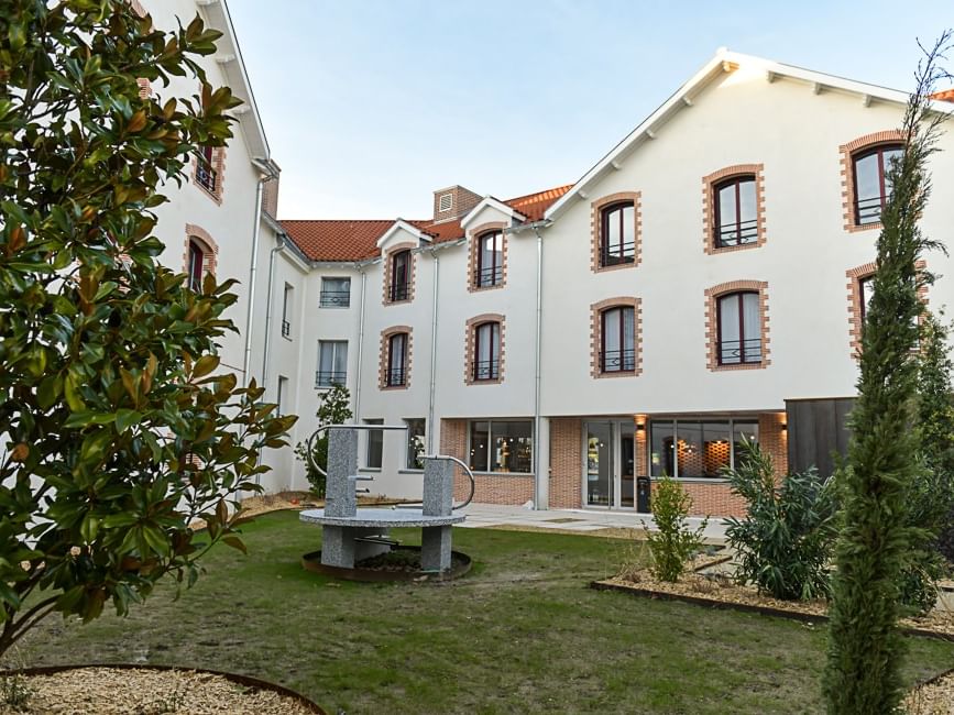 Extérieur de l'Hôtel Rivella avec pelouse et sculpture en pierre.