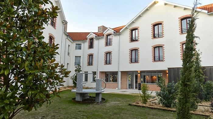 Extérieur de l'Hôtel Rivella avec pelouse et sculpture en pierre.