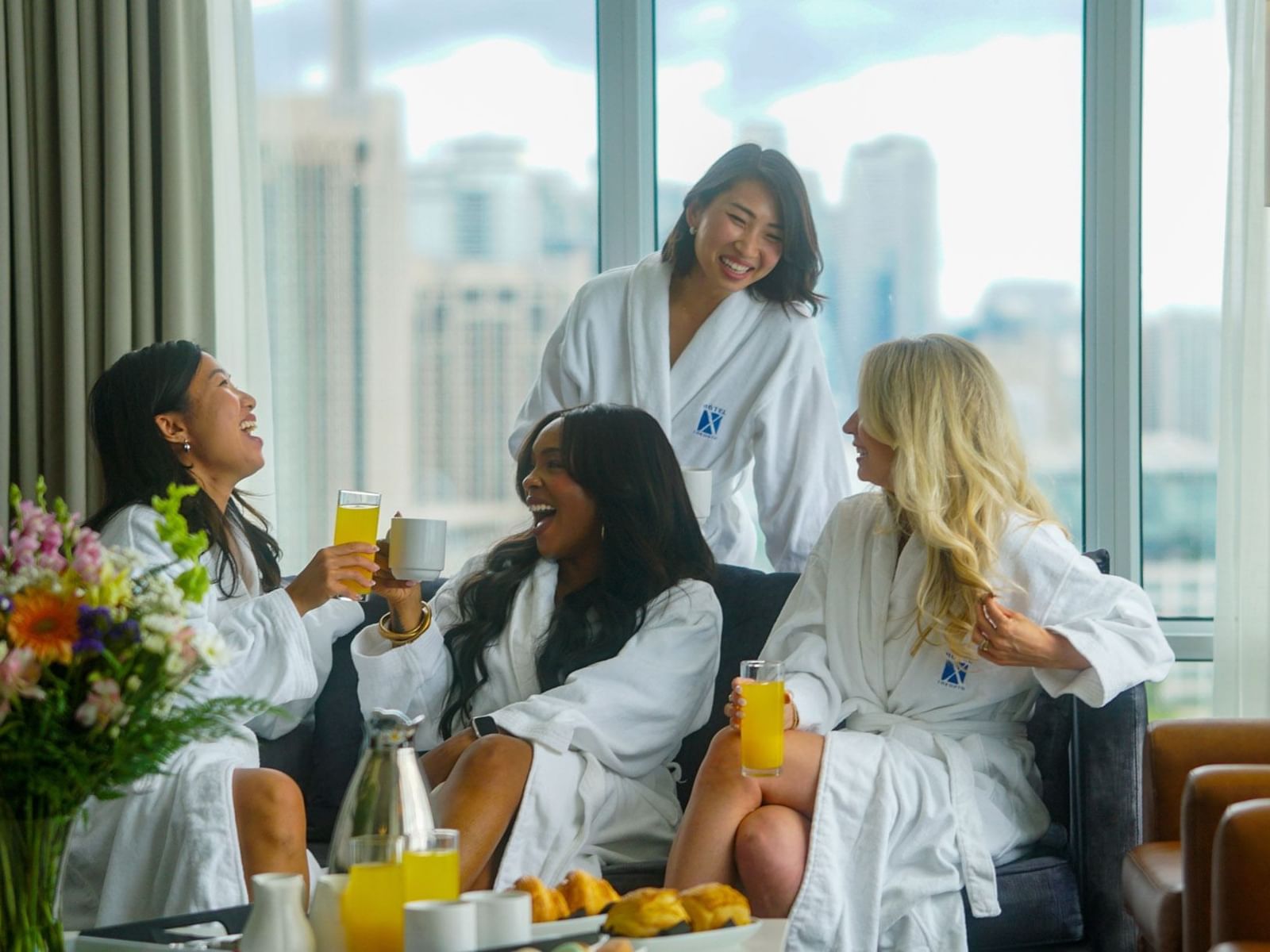 Girls in white robes enjoying drinks in a room with a view featuring the Girls Getaway Package at Toronto x Hotel