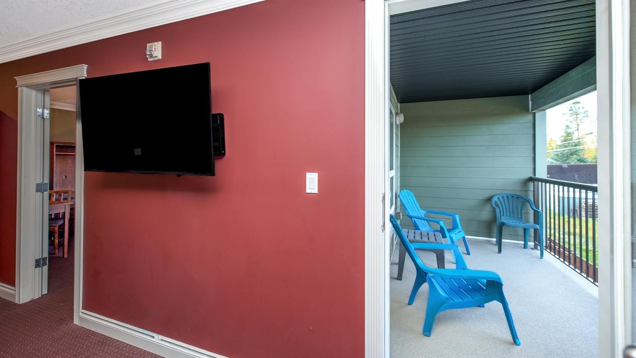 Guest room with coral accent wall, wall-mounted TV, and private balcony with blue chairs at Coast Edson Hotel.