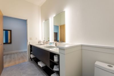 Bathroom vanity with illuminated mirrors and dark wood cabinetry in Dunedin hotel rooms at The J Hotel
