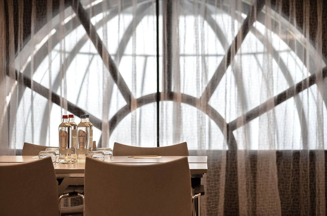 Empty meeting table with water bottles and chairs in front of arched window at Hotel Barsey by Warwick 