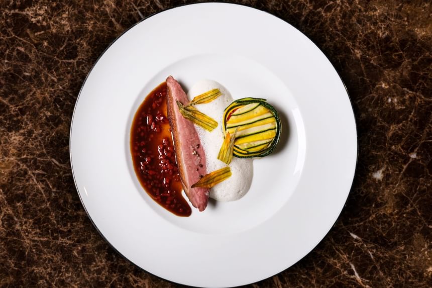Gourmet dish with seared duck breast, a vibrant berry sauce, and a colorful zucchini tart in Square One at Park Hyatt Saigon