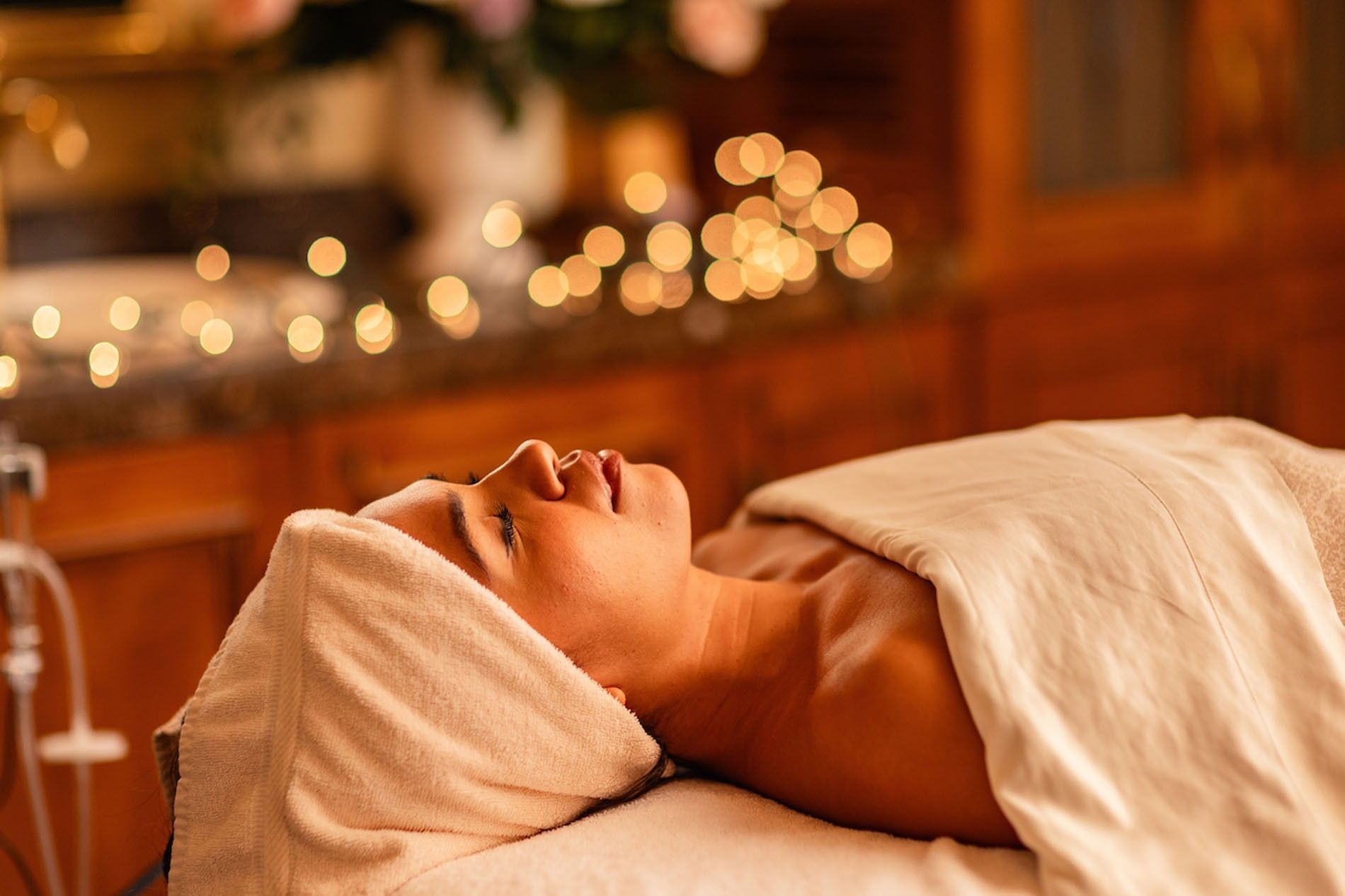 Relaxed woman receiving Fountain of Youth Signature Treatment with soft bokeh background lights and towels at Kelly's Spa