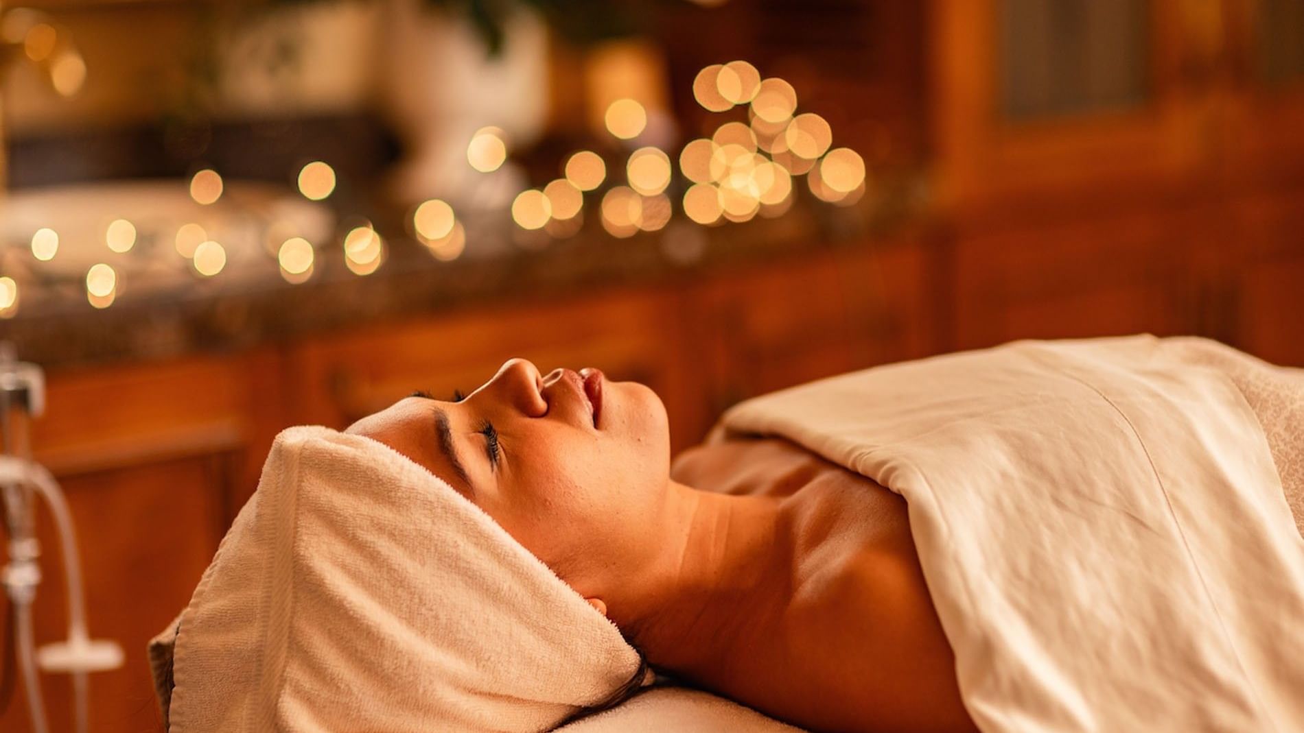 Relaxed woman receiving Fountain of Youth Signature Treatment with soft bokeh background lights and towels at Kelly's Spa