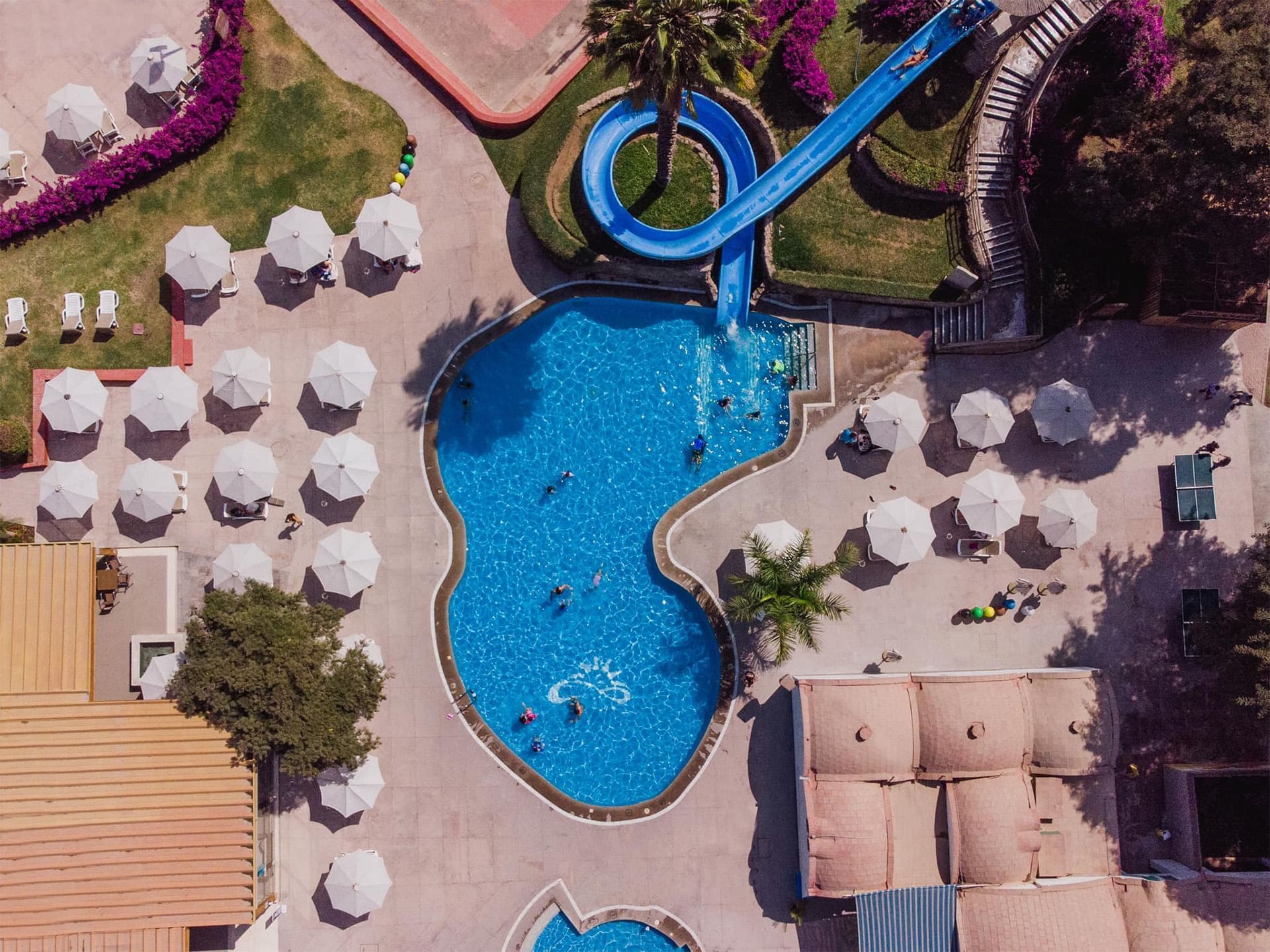 Aerial view of pool with a slide, surrounded by umbrellas & green lawns at Las Dunas Resort Ica Peru Hotels