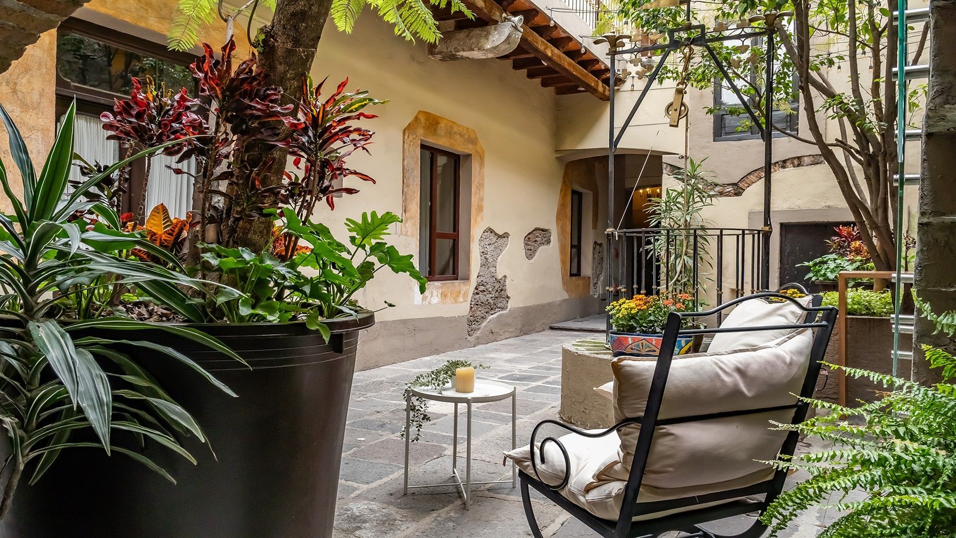 Cozy outdoor patio with potted plants, a cushioned chair, and a small side table at Quinta Real Puebla