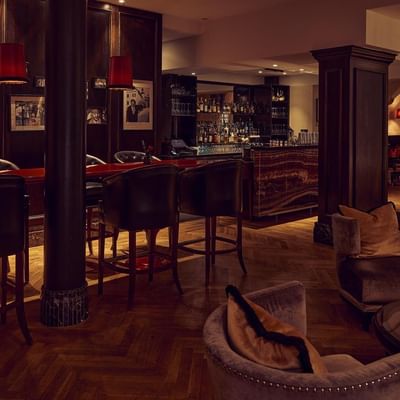 Elegante Bar mit roten Sesseln, Tischen, dunklen Säulen und kunstvollen Rahmen an den Wänden.