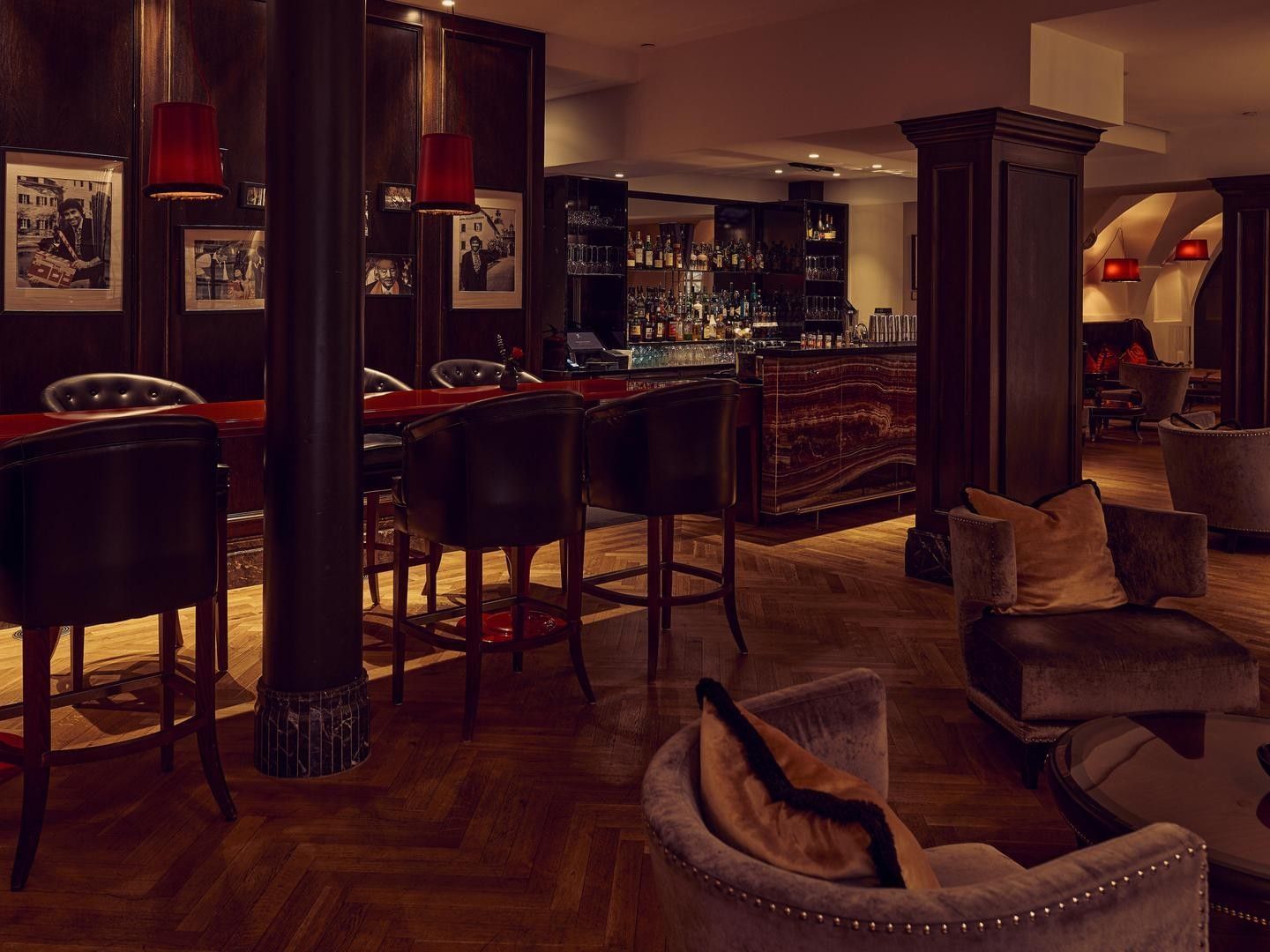 Elegante Bar mit roten Sesseln, Tischen, dunklen Säulen und kunstvollen Rahmen an den Wänden.