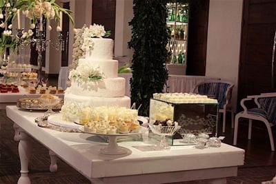 A beautiful multi-tiered white wedding cake with white flower decorations on a dessert table at Hotel Mykonos