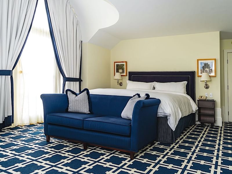 Comfortable hotel room at El Prado Hotel, featuring a large bed and a vibrant blue sofa with pillows