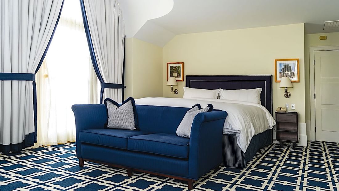 Cozy sofa and nightstand by the bed in Grand Deluxe Suite with geometric patterned carpet at El Prado Hotel