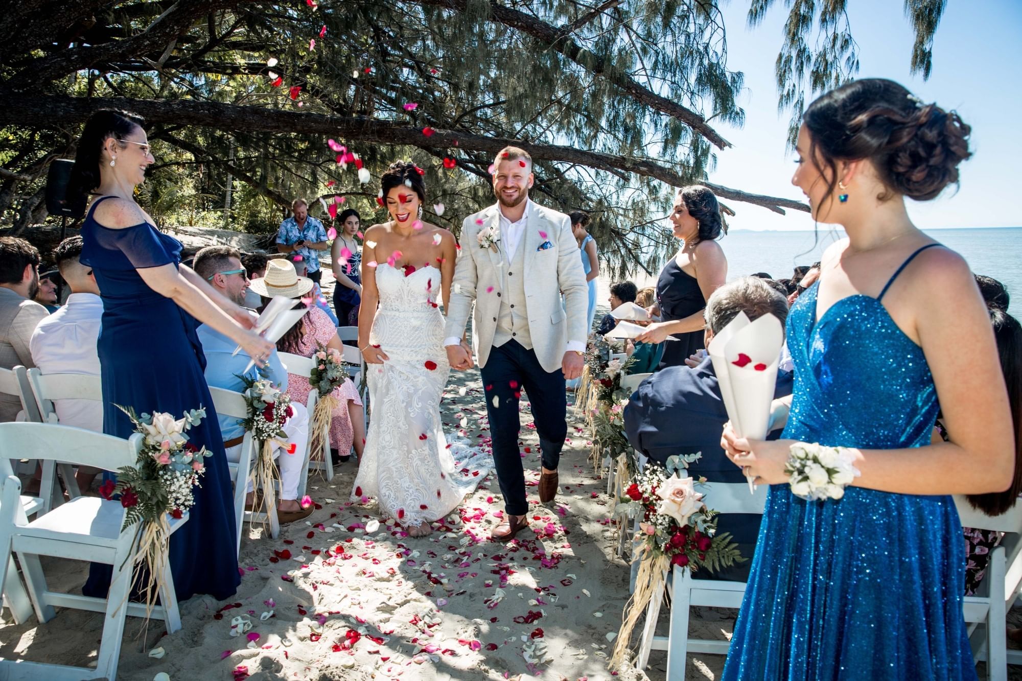 Couple walking with guests seated on chairs & petals on sand in Four Mile Beach at Pullman Port Douglas Sea Temple Resort & Spa