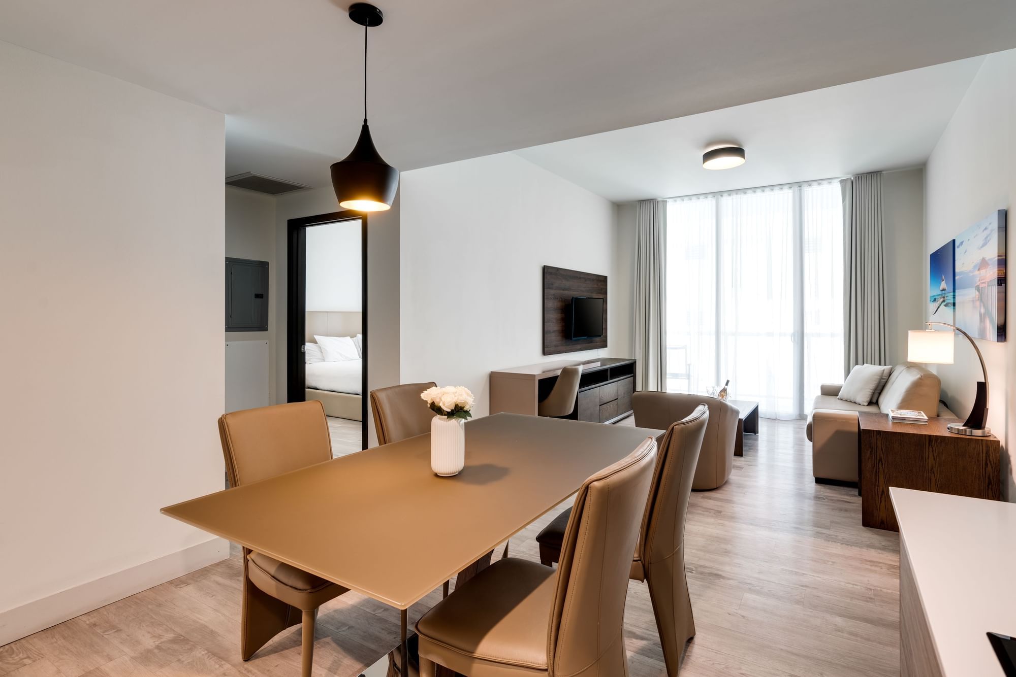A wide view of a modern hotel suite with a dining area, living room, and large windows.