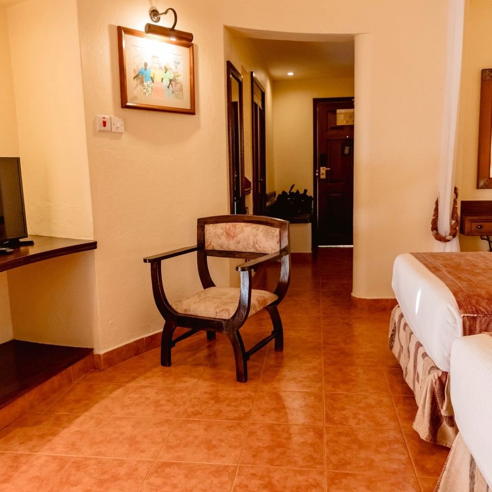 Two beds, chair, TV, and mirror in Standard Twin Room at Arusha Serena Hotel in Arusha.