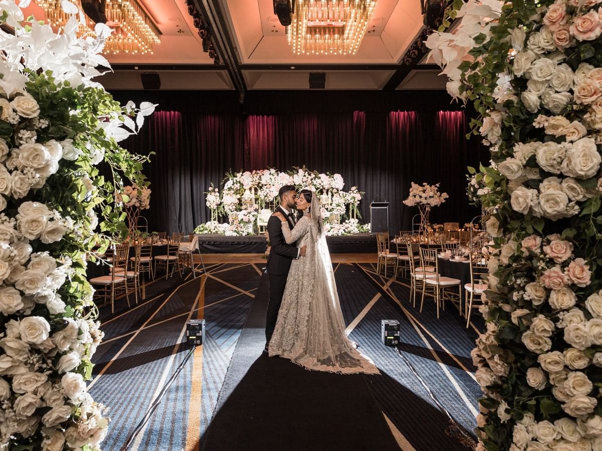 Couple embracing at their wedding aisle surrounded by white floral arrangements in Sofitel Brisbane Central
