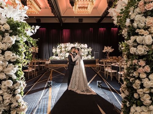 Couple embracing at their wedding aisle surrounded by white floral arrangements in Sofitel Brisbane Central