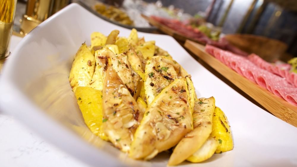 Grilled yellow squash in a white bowl by a buffet spread in Abbiocco at Warwick Paradise Island Bahamas