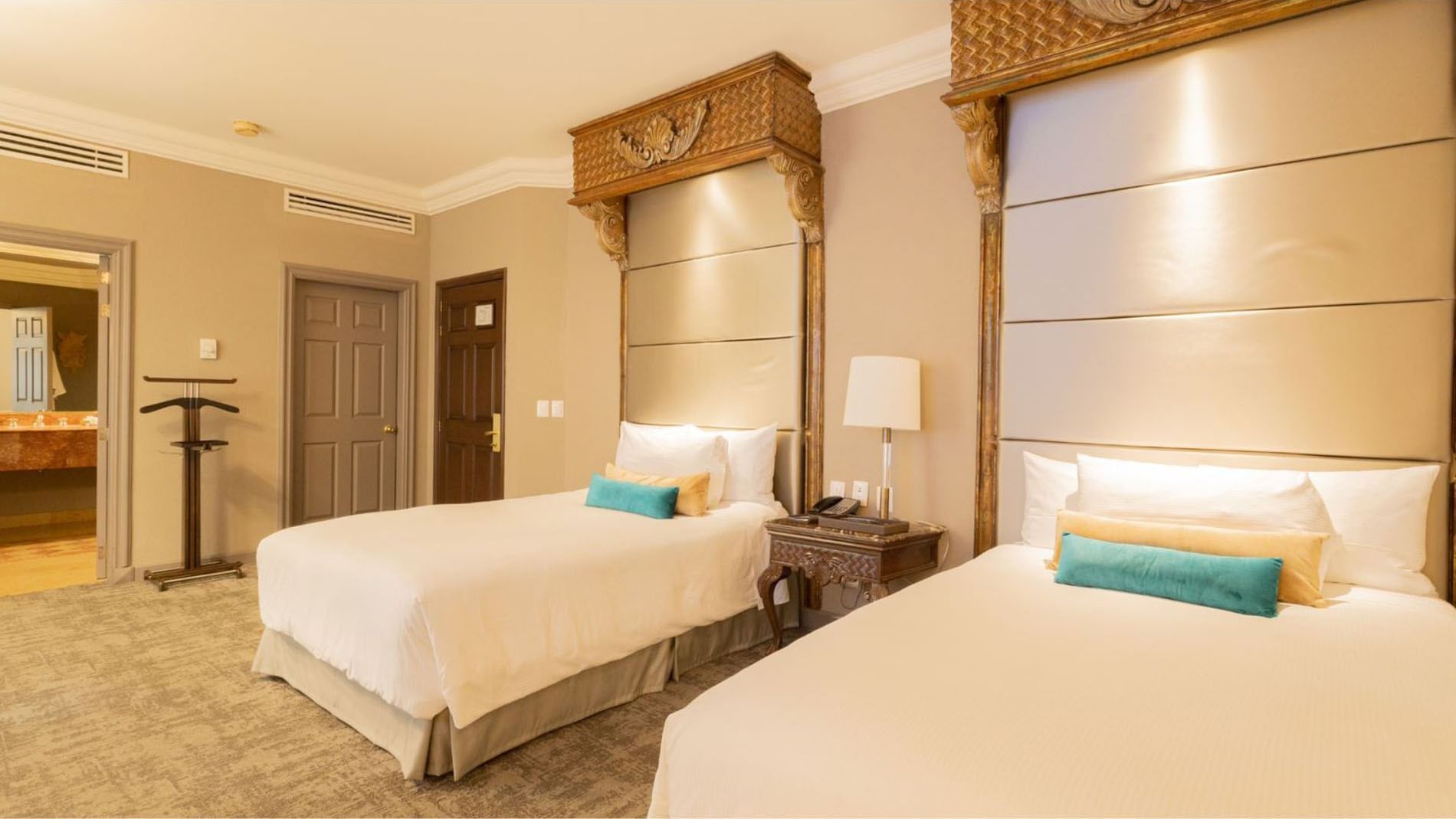 2 Double Master Suite with ornate wood carvings featuring teal accent pillows and lamps at Quinta Real Monterrey