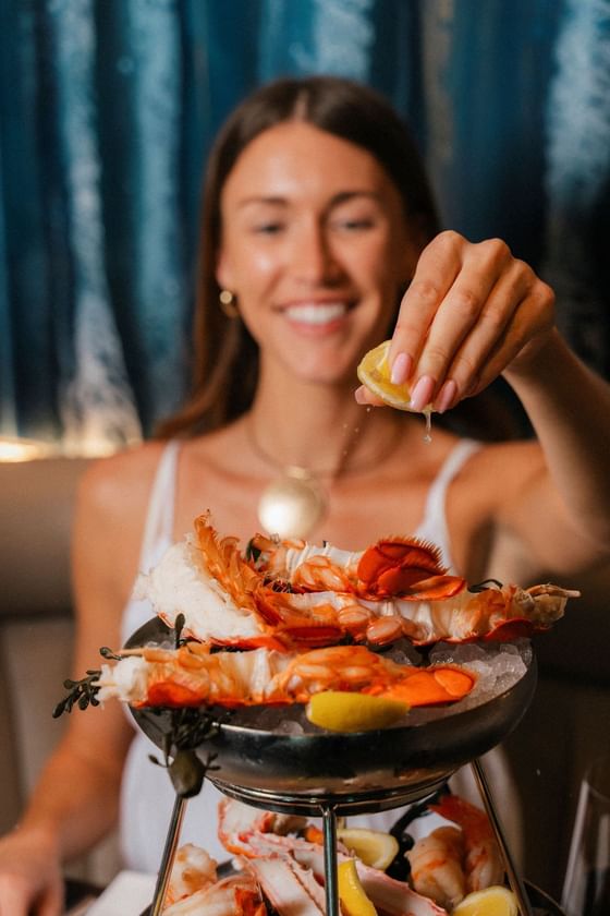Woman smiling and squeezing lemon over a plate of seafood on a tiered serving dish.