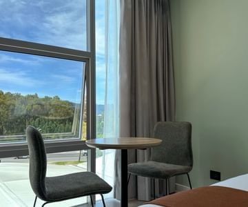 Pair of chairs and a small round table beside an open window overlooking green scenery at Unika Hotels